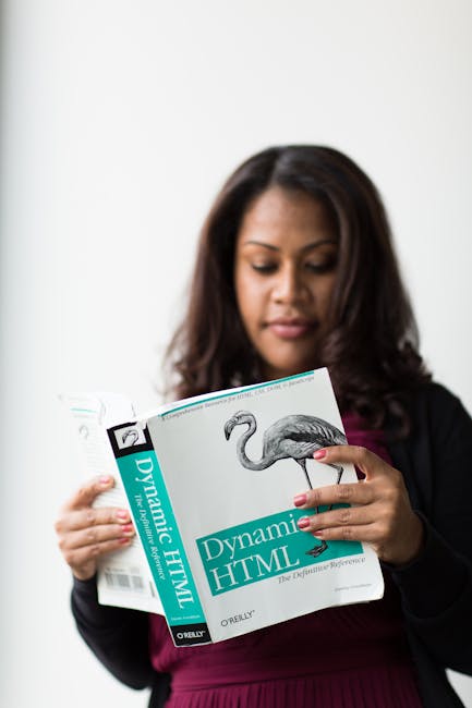 A woman with medium-dark skin and long, dark hair is holding a book titled 'Dynamic HTML' by O'Reilly, with her left hand gripping the lower part of the front cover and her right hand supporting the b